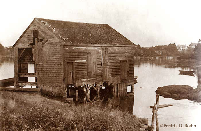 Israel Forster’s Grist Mill  sat over Bennetts Brook on pilings. Manchester Harbor is behind it, with the town in the distance. Later, the mill was converted to produce furniture turnings (shaped parts of furniture, such as table legs).